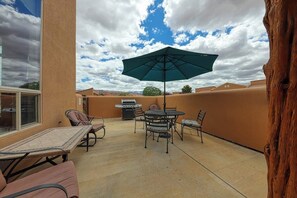 An outdoor patio with a table and chairs, a grill, and a large umbrella. - Lovely 3BR Mountainview with Pool and Hot Tub (Moab)