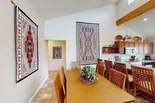 A dining area with a long wooden table and chairs, a potted plant, and two large wall hangings. - Comfortable Home with Mountain Views and Shared Seasonal Hot Tub and Pool (Moab)