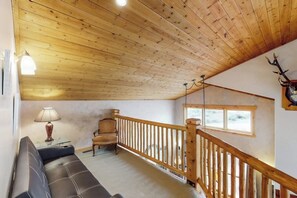 Un soffitto in legno, un divano, una poltrona, una lampada, una finestra e un cervo appeso al muro.