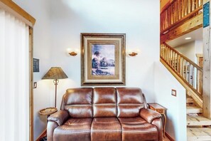 A room with a brown leather sofa, a framed picture on the wall, a lamp, and a wooden staircase. - Luxury Home with Spectacular Views and Hot Tub - Walk to Golf Course (Moab)