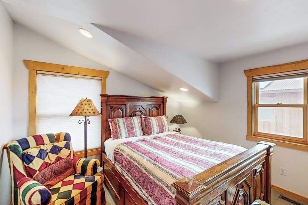 Un dormitorio con una cama de madera, un sillón colorido y una ventana con persianas.