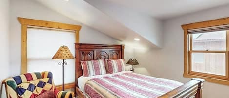 Un dormitorio con una cama de madera, un sillón colorido y una ventana con persianas.