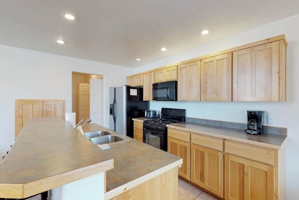 A modern kitchen with wooden cabinets, a stainless steel refrigerator, a microwave, a stove, and a coffee maker. - Spacious Townhome in a Great Location with Seasonal Shared Pool and Hot Tub (Moab)
