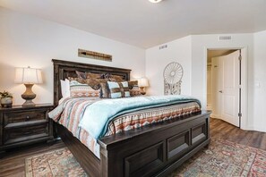 A bedroom with a dark wooden bed, patterned bedding, two bedside tables with lamps, a decorative wall piece, and a patterned rug. - Cozy 3BR Moab Condo with Pool Hot Tub and Mountain Views near Arches (Moab)