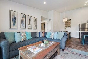 A modern living room with a grey sofa, wooden coffee table, and a kitchen area in the background. - Cozy 3BR Moab Condo with Pool Hot Tub and Mountain Views near Arches (Moab)