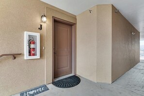 Paredes externas bege com uma porta marrom, um extintor de incêndio emoldurado e um tapete de entrada com a palavra 'home'.