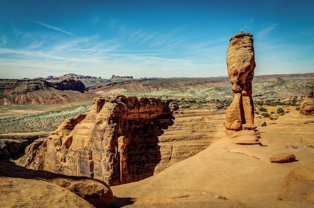 A natural rock formation with a prominent vertical rock in the foreground and a layered cliff in the background.