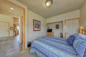 A bedroom with a large bed, a television on a wooden stand, and a door leading to a bathroom. - Charming Condo with Mountain Views and Seasonal Pool & Hot Tub - Close to Town (Moab)