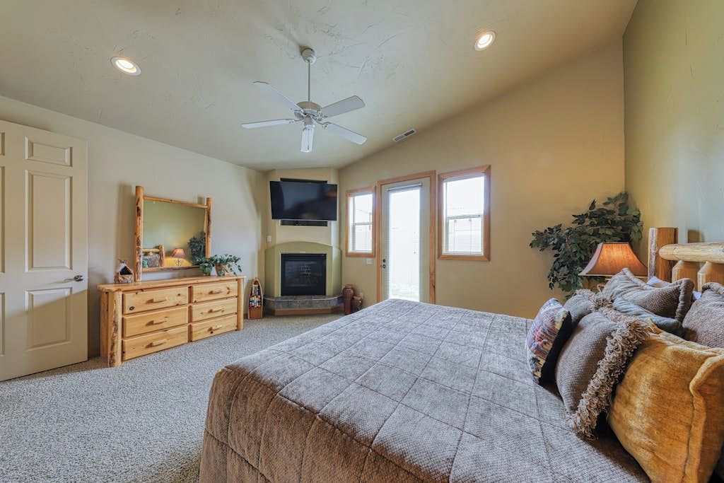 A bedroom with a bed, dresser, television, fireplace, and a ceiling fan.