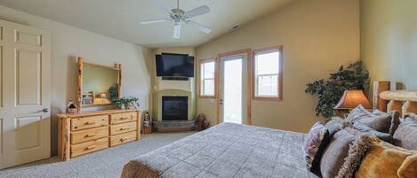 A bedroom with a bed, dresser, television, fireplace, and a ceiling fan.