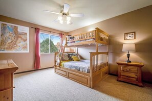 Een slaapkamer met stapelbedden, een plafondventilator, een bureau, een lamp en een raam met gordijnen.