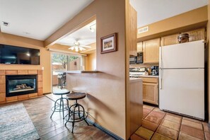 A kitchen with a refrigerator, microwave, and stove. There is a bar area with stools and a television mounted above the fireplace. - Lovely Townhome with Shared Pool - Dog Friendly (Moab)