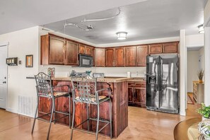 A kitchen with wooden cabinets, a stainless steel refrigerator, and a bar area with metal chairs. - Lovely Moab Home with Shared Pool Hot Tub and Stunning Desert Mountain Views (Moab)