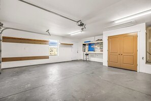 A spacious, well-lit room with a concrete floor, a wooden door, and a window with a poster. - Lovely Moab Home with Shared Pool Hot Tub and Stunning Desert Mountain Views (Moab)