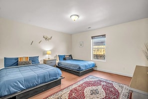 A bedroom with two beds, a red patterned rug, a window with blinds, and a wall-mounted light fixture. - Lovely Moab Home with Shared Pool Hot Tub and Stunning Desert Mountain Views (Moab)