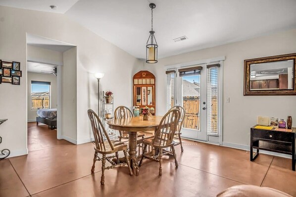 A dining area with a wooden table and chairs, a hanging light fixture, and a view through a glass door. - Lovely Moab Home with Shared Pool Hot Tub and Stunning Desert Mountain Views (Moab)