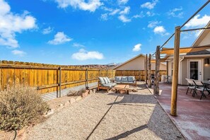 An outdoor patio area with a wooden fence, a seating arrangement, and a building in the background. - Lovely Moab Home with Shared Pool Hot Tub and Stunning Desert Mountain Views (Moab)