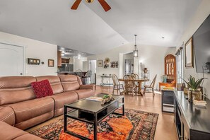 A spacious living room with a brown leather sofa, a coffee table, and a dining area with chairs and a table. - Lovely Moab Home with Shared Pool Hot Tub and Stunning Desert Mountain Views (Moab)