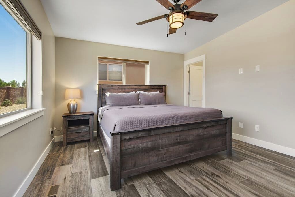 A bedroom with a bed, a nightstand, a ceiling fan, and a window.