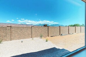 A view through a window of a brick wall with a clear sky and distant mountains. - Comfortable Moab Condo with Patio and Views - Close to Arches and Downtown (Moab)