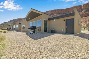 A modern building with a gravel driveway, large windows, and a barbecue area. - Comfortable Moab Condo with Patio and Views - Close to Arches and Downtown (Moab)