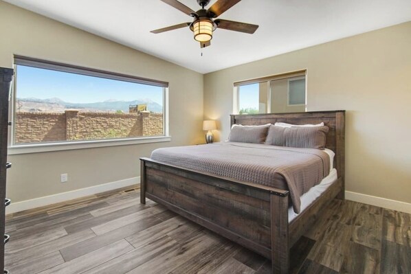 A bedroom with a large window, a bed, a ceiling fan, and a nightstand. - Comfortable Moab Condo with Patio and Views - Close to Arches and Downtown (Moab)