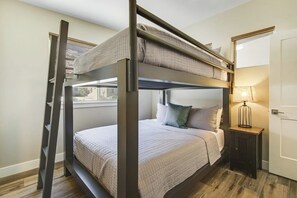 A bunk bed room with a ladder, a bedside table with a lamp, and a door. - Comfortable Moab Condo with Patio and Views - Close to Arches and Downtown (Moab)