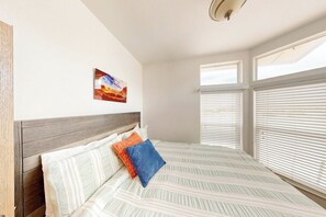 A bedroom with a bed, a headboard, a window with blinds, and a wall-mounted artwork.