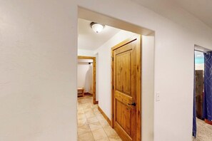A hallway with a wooden door, a tiled floor, and a ceiling light.