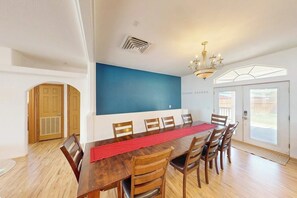 A dining area with a long wooden table, multiple chairs, a red runner, and a chandelier.