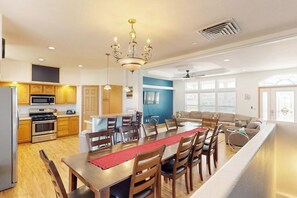 A modern kitchen with wooden cabinets, stainless steel appliances, and a dining area with a long table and chairs.