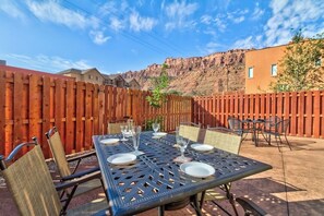 Eine Terrasse im Freien mit Esstisch und Stühlen, vor einer Holzzaun und einer Berglandschaft.
