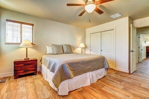 Ein Schlafzimmer mit einem Bett, Nachttischlampen, einem Holznachttisch, einem Deckenventilator und einer Tür zu einem anderen Raum.