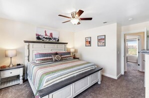 A bedroom with a bed, a nightstand, a lamp, a ceiling fan, and a door leading to another room. - Adventure Ready Moab Townhouse with Pool and Hot Tub Access - Close to Utah's national parks (Moab)