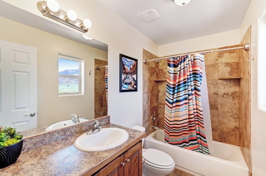 A bathroom with a sink, mirror, and a shower with a striped curtain.