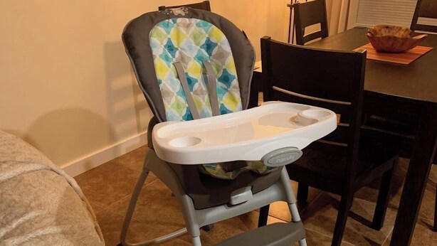 En babystol med bakke placeret i et spiseområde med stole og et bord.