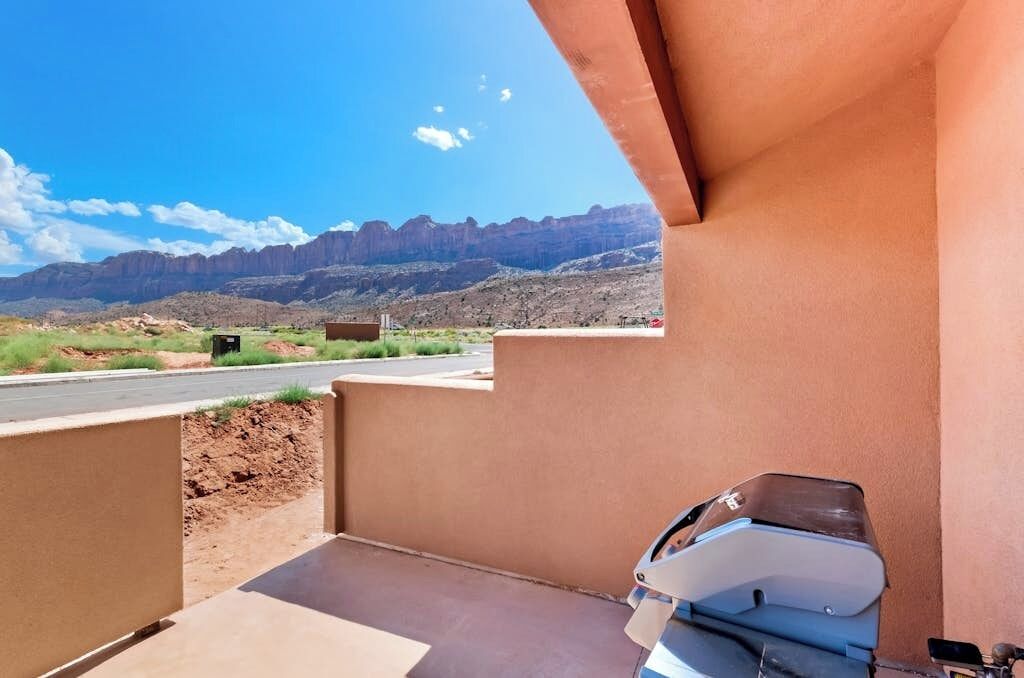 A balcony with a barbecue grill, a view of a road, and distant mountains.