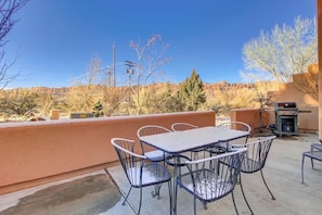 An outdoor patio with a table and chairs, a barbecue grill, and a view of a mountainous landscape. - Golf Course Front Condo with Seasonal Pool & Views - Walk to Steel Bender Trail (Moab)