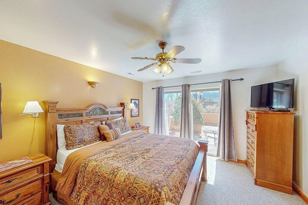 A hotel room with a bed, a ceiling fan, a TV, and a balcony with curtains.