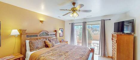 A hotel room with a bed, a ceiling fan, a TV, and a balcony with curtains.