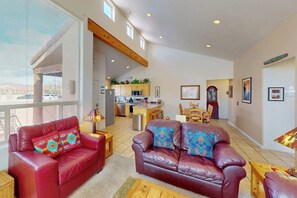 A spacious living area with a red leather sofa, a brown leather sofa, and a wooden coffee table. There is a kitchen in the background with a dining table and chairs. - Spacious Family Friendly Home near Downtown with Seasonal Pool & Hot Tub (Moab)