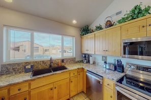 A kitchen with wooden cabinets, a granite countertop, a stainless steel oven, and a window with blinds. - Spacious Family Friendly Home near Downtown with Seasonal Pool & Hot Tub (Moab)