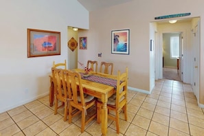 A dining area with a wooden table and chairs, a tiled floor, and framed artwork on the walls. - Spacious Family Friendly Home near Downtown with Seasonal Pool & Hot Tub (Moab)