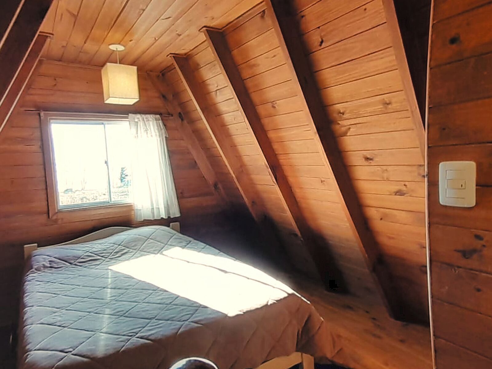 Una habitación con cama, ventana con cortinas y lámpara.