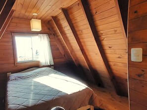 Una habitación con cama, ventana con cortinas y lámpara.