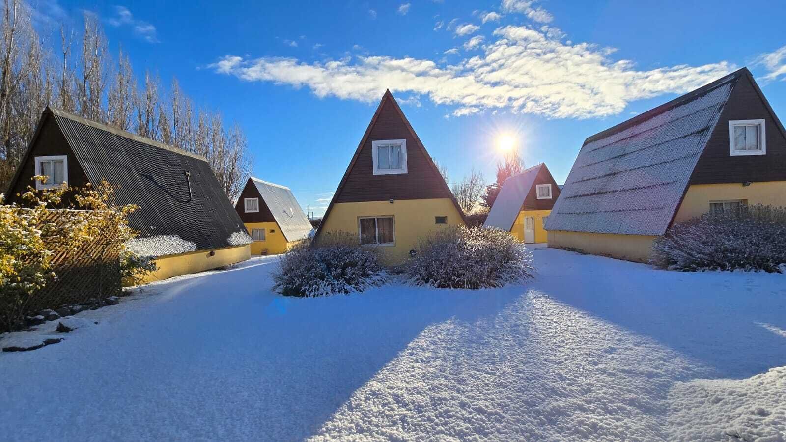 Una hilera de casas tipo chalet con techos inclinados, rodeadas de nieve y vegetación escasa.