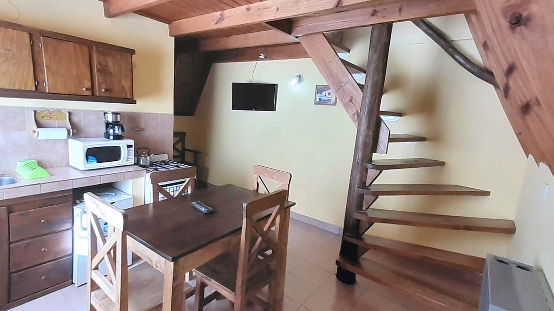 Una cocina compacta con comedor, una escalera de madera y un televisor pequeño.