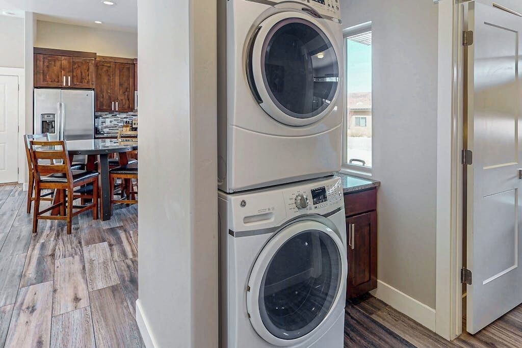 A laundry room with stacked washers and dryers, wooden cabinets, and a dining area with a table and chairs.