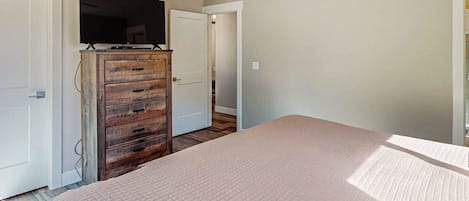 Un dormitorio con cama, cómoda de madera, televisor y puerta que da a otra habitación.