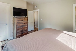 A bedroom with a bed, a wooden dresser, a television, and a door leading to another room. - Tranquil 2BR Mountainview Rim View with Hot Tub (Moab)